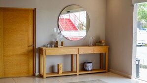 Una consola de madera con un espejo encima, un pequeño estante y una puerta a la izquierda.