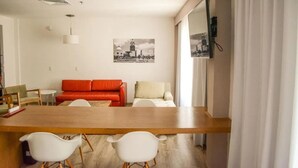 Una sala de estar moderna con una mesa de comedor de madera, dos sillas blancas, un sofá rojo y una mesita redonda.