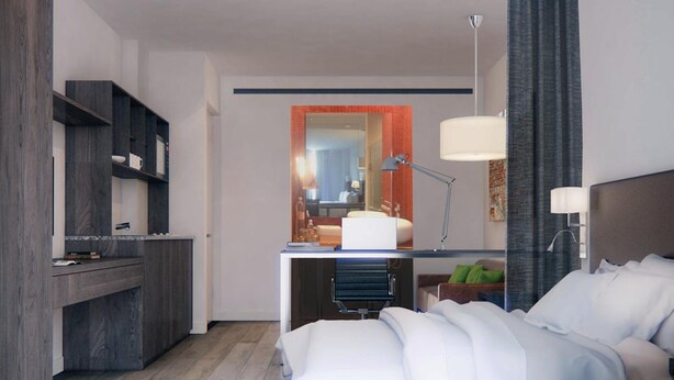 Habitación de hotel moderna con cama, mesita de noche, lámpara y vista al baño a través de un separador de vidrio.