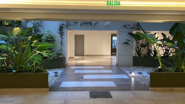 Eine moderne Lobby mit einem 'SALIDA'-Schild, Topfpflanzen und einem gefliesten Boden, der zu einem Aufzug führt.