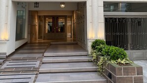 Ein Gebäudeeingang mit der Nummer „1557“ über der Tür, eine Treppe, die zum Eingang führt, und eine kleine Gartenanlage mit Pflanzen zur Rechten.