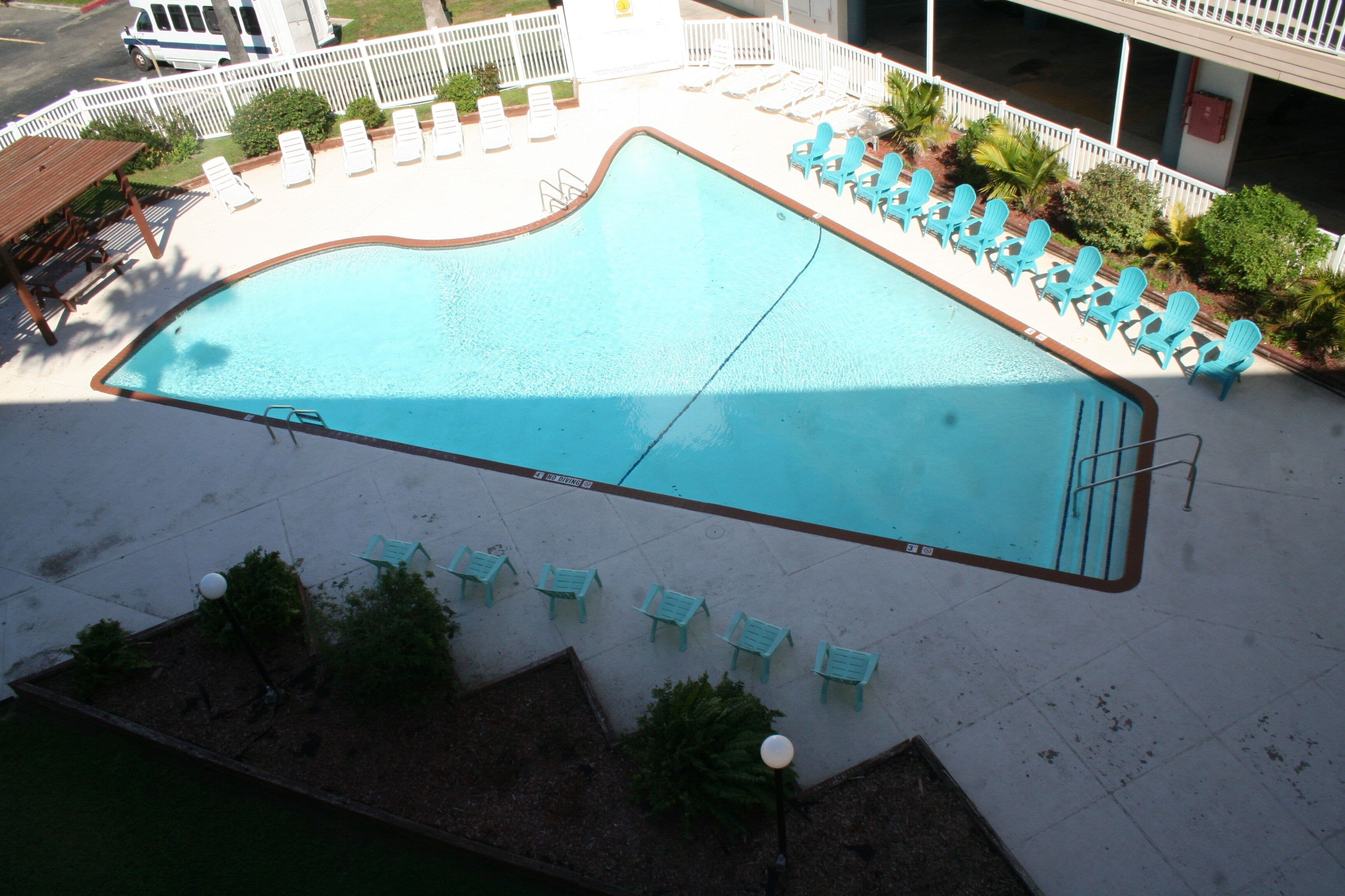 A swimming pool with a wavy edge, surrounded by a white fence and multiple lounge chairs.