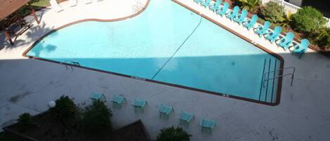 A swimming pool with a wavy edge, surrounded by a white fence and multiple lounge chairs.