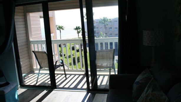 A room with a sliding glass door leading to a balcony with a white railing and two chairs. - Beach Condo Walk to the sand beach and Texas State Aquarium. (Corpus Christi)