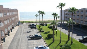 A parking lot with several cars, a building with balconies, and a view of the beach and ocean. - Beach Condo Walk to the sand beach and Texas State Aquarium. (Corpus Christi)
