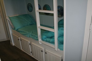 Uma cama beliche com compartimento inferior, estrutura branca e roupa de cama verde-água.