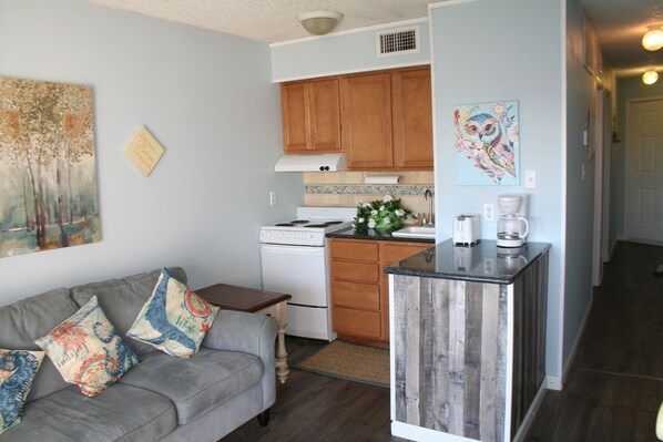 A compact kitchen with wooden cabinets, a white stove, and a coffee maker. - Beach Condo Walk to the sand beach and Texas State Aquarium. (Corpus Christi)