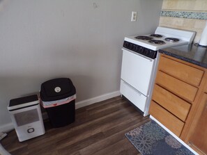Una cocina compacta con estufa blanca, un bote de basura y gabinetes de madera.
