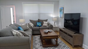 A living room with a grey sofa, a coffee table, a TV, and a window with blinds. - Arlington Park Area! Heated Pool 3 bedroom/ 2 bath (Sarasota)
