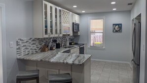 A kitchen with white cabinets, a marble countertop, and a built-in microwave. There are two stools and a window with blinds. - Arlington Park Area! Heated Pool 3 bedroom/ 2 bath (Sarasota)
