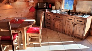 Une cuisine rustique aménagée dans une cabane en bois, avec une table à manger, des chaises, un poêle et un évier.