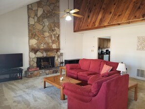 A living room with a stone fireplace, a red sofa, a wooden coffee table, and a ceiling fan.