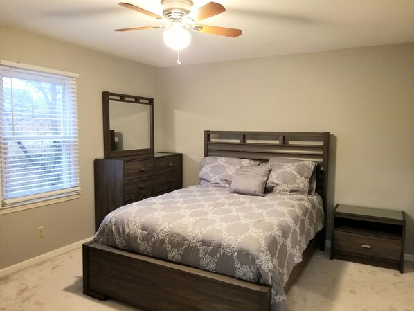 A bedroom with a bed, dresser, nightstand, and ceiling fan.