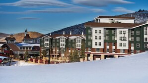 Un hotel a più piani con una seggiovia sullo sfondo, circondato da colline innevate.