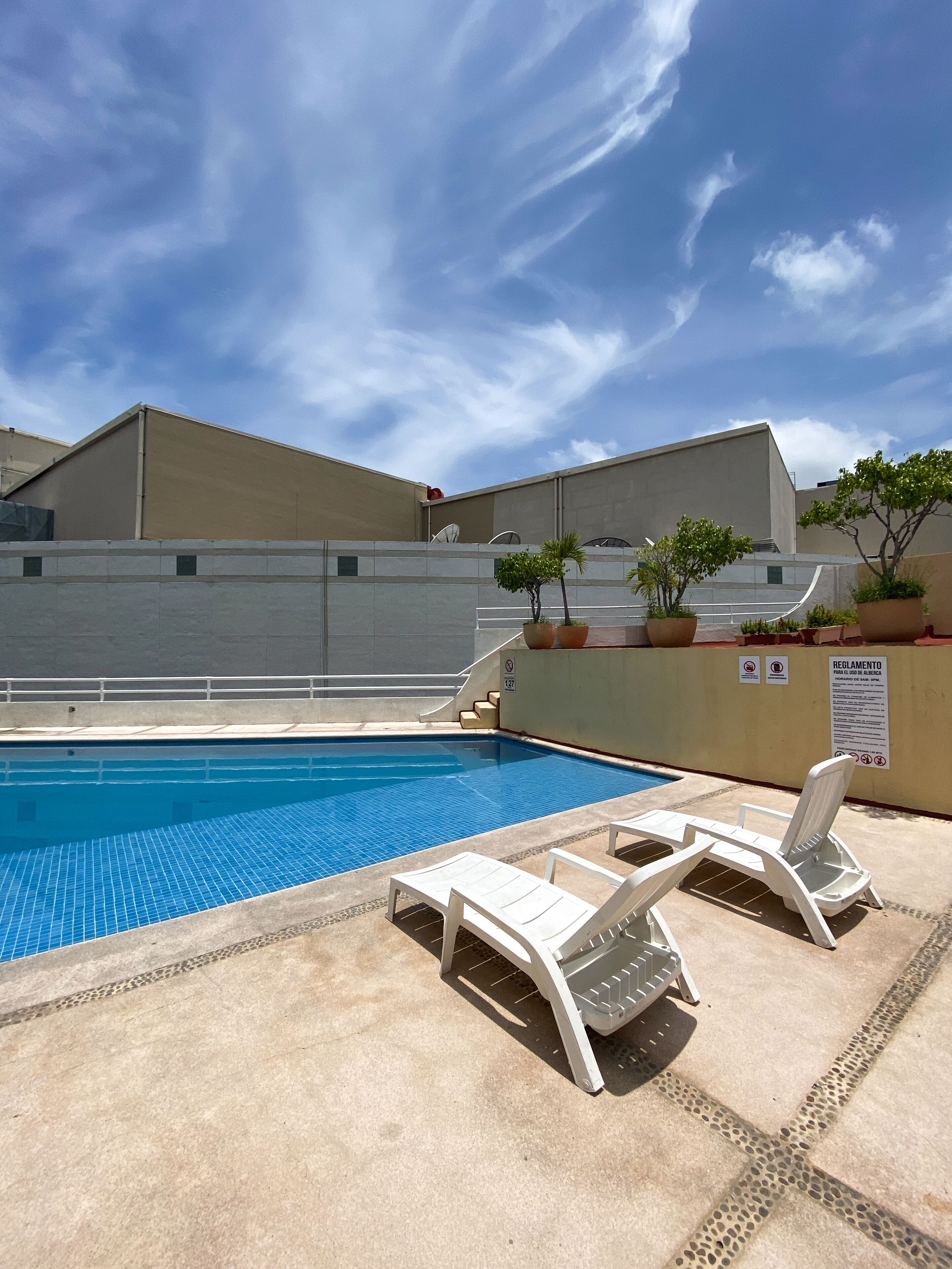 A swimming pool with clear blue water, surrounded by white lounge chairs and potted plants.