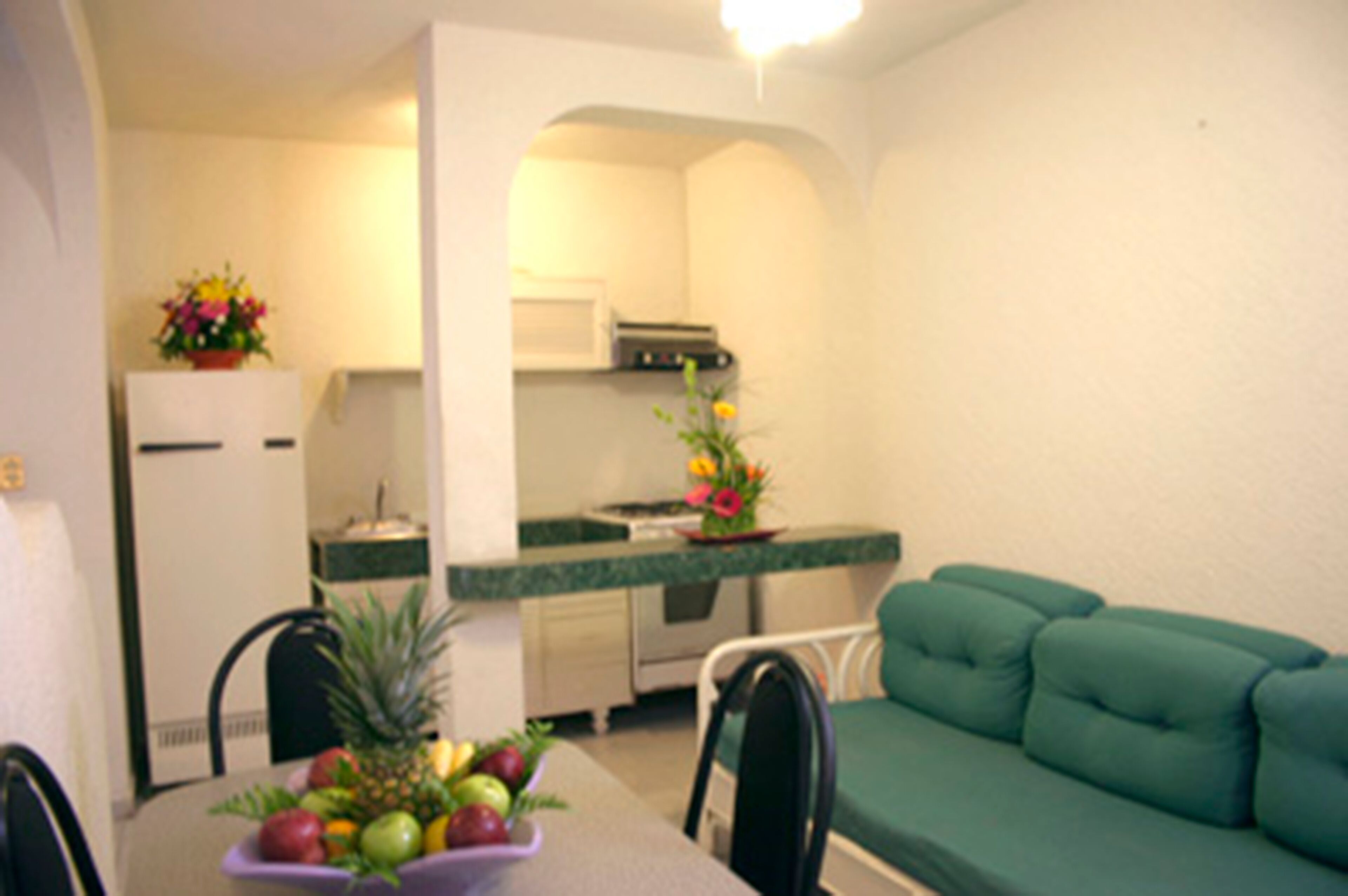 Un espacio habitable compacto con una mesa de comedor para dos personas, un sofá verde, una zona de cocina con microondas y refrigerador.
