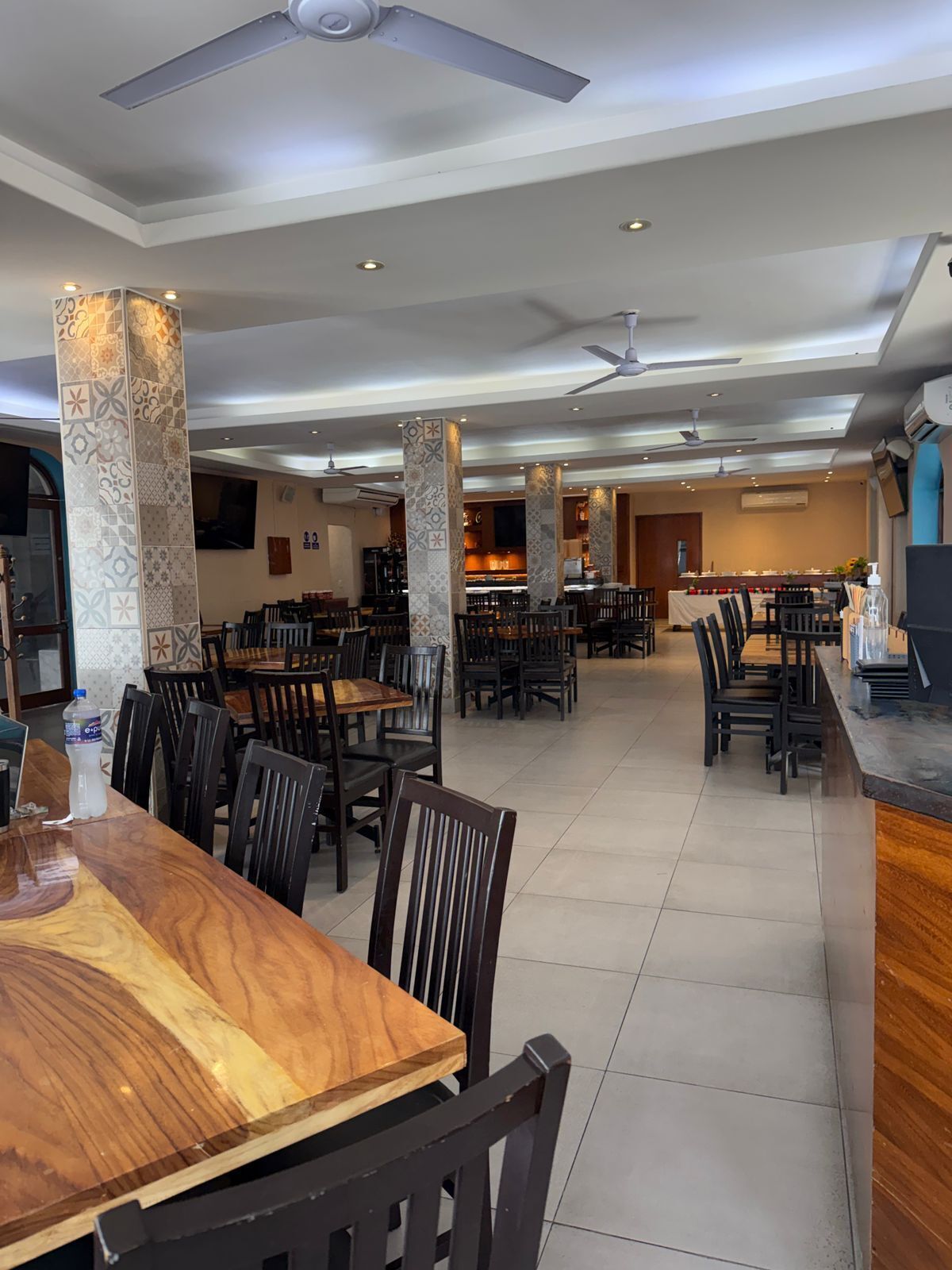 Een ruim restaurant met meerdere eettafels en stoelen, plafondventilatoren en een bar.