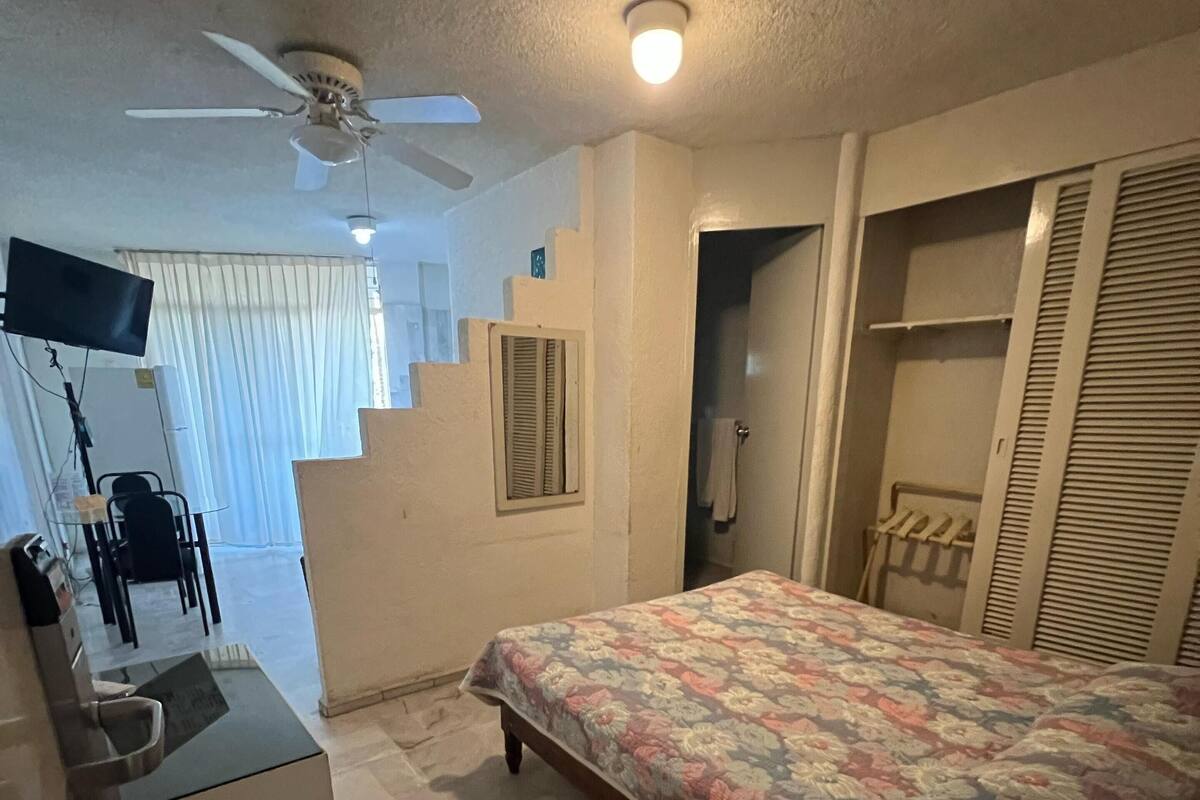 Ein Schlafzimmer mit einem Bett, einem Schreibtisch, einem Sessel, einem Deckenventilator und einer Treppe.