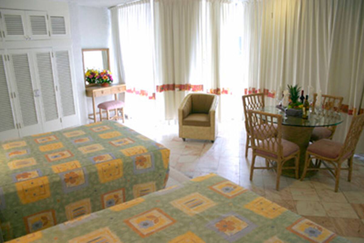 Ein Hotelzimmer mit zwei Betten, einer Sitzecke mit Sessel und Tisch, einem Fenster mit Vorhängen und Blick ins Freie.