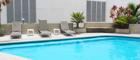 A swimming pool with lounge chairs and potted plants.