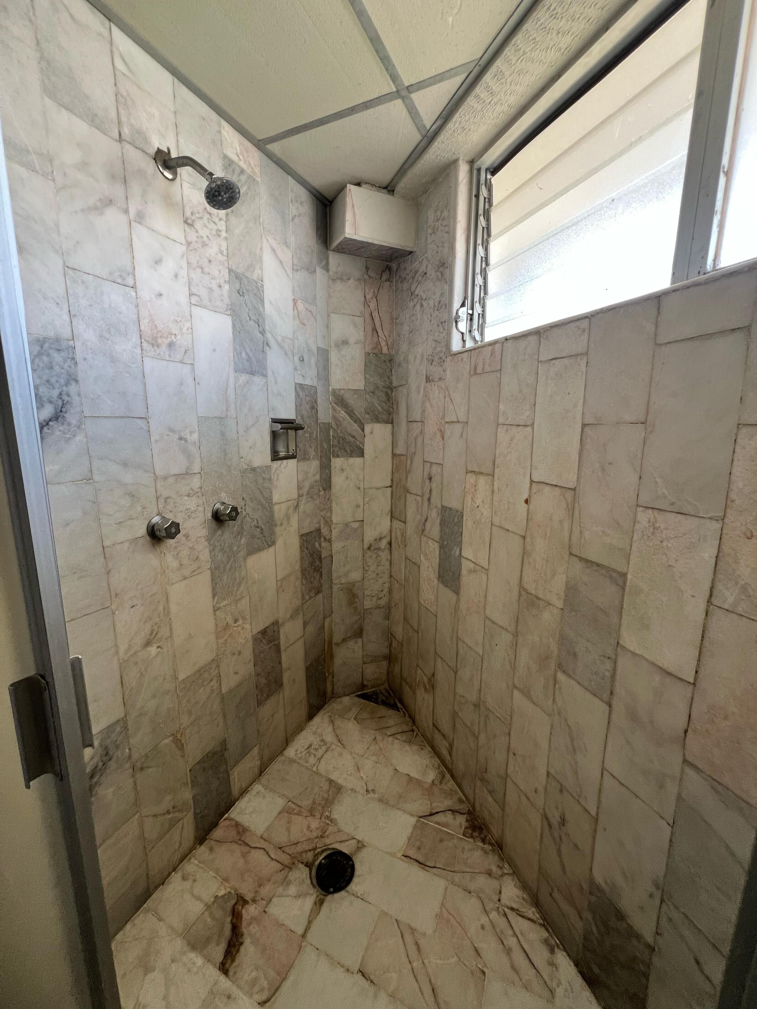 A small, tiled shower area with a window and a metal handle.