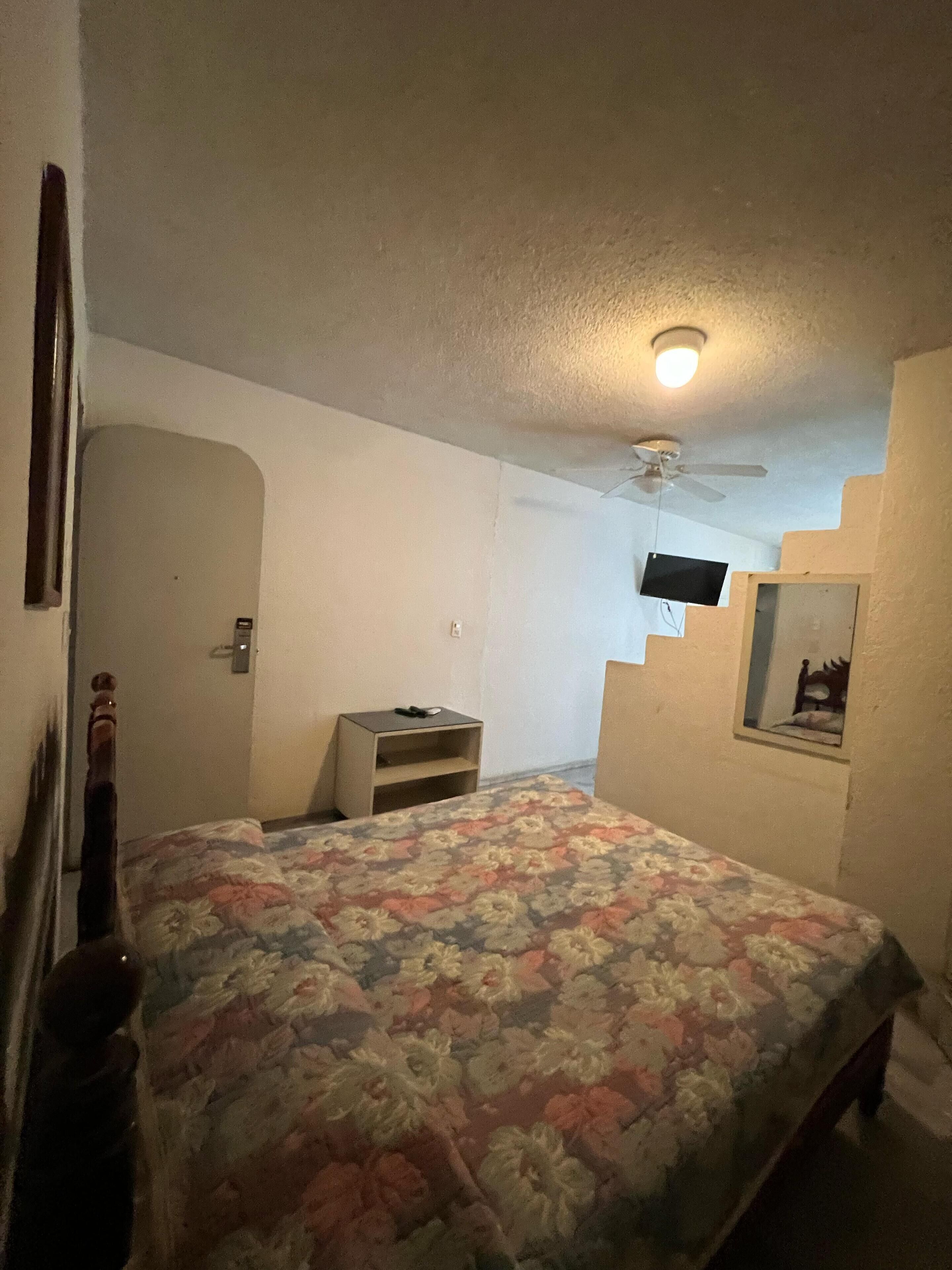 Ein Schlafzimmer mit einem Bett, einem Nachttisch, einem an der Wand montierten Fernseher und einem Deckenventilator.