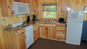 A kitchen with wooden cabinets, a microwave, stove, sink, and refrigerator. - Cottage #25 - 1 bedroom/ 1 bath (Cape Vincent)