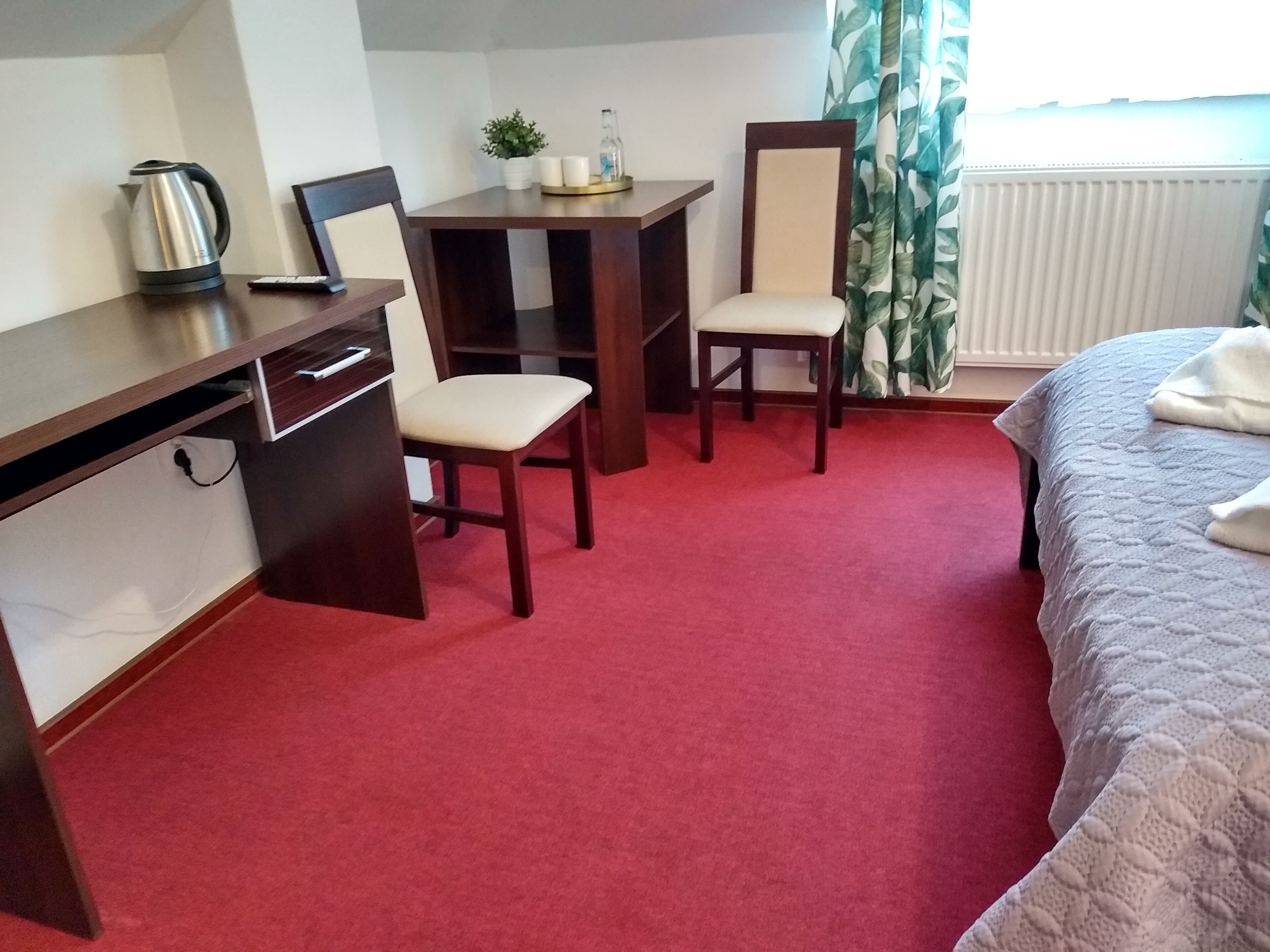 A hotel room with a desk, two chairs, a bed, and a radiator.