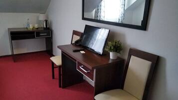 Quarto de hotel com escrivaninha, duas cadeiras, televisão, uma pequena planta em vaso e um espelho na parede.