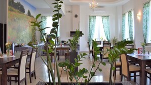A dining area with a large painting on the wall, a chandelier, and multiple dining tables with chairs. - Hotel Zlotogorski (gmina Koscielec)