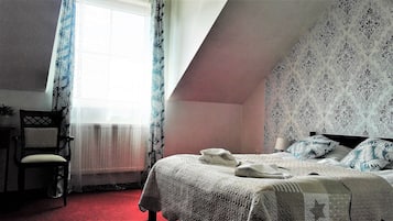 Un dormitorio con cama, una silla, un ventanal con cortinas y una pared con diseño.