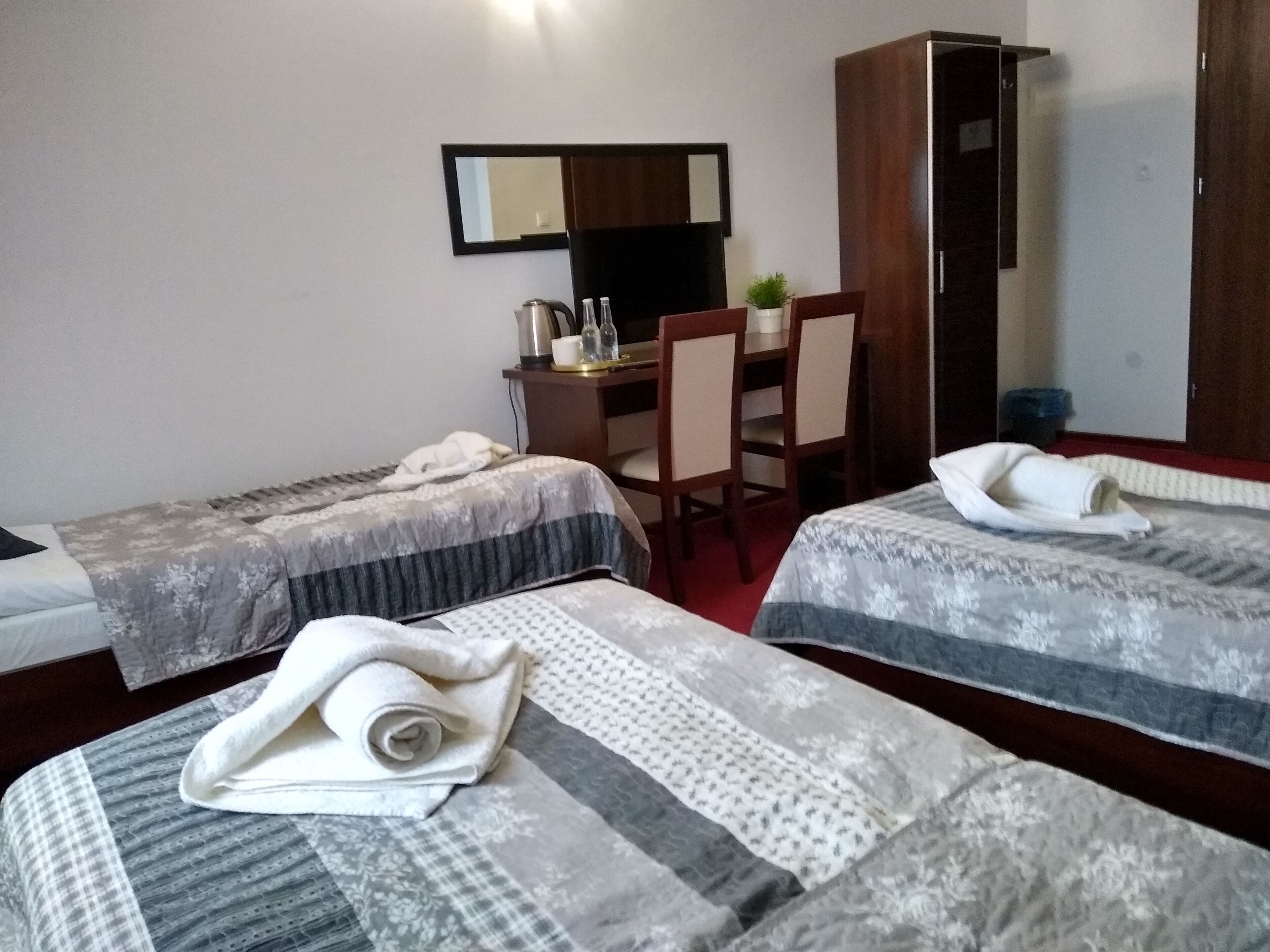 Ett hotellrum med två separata sängar, ett skrivbord med en stol, en garderob och en spegel på väggen.