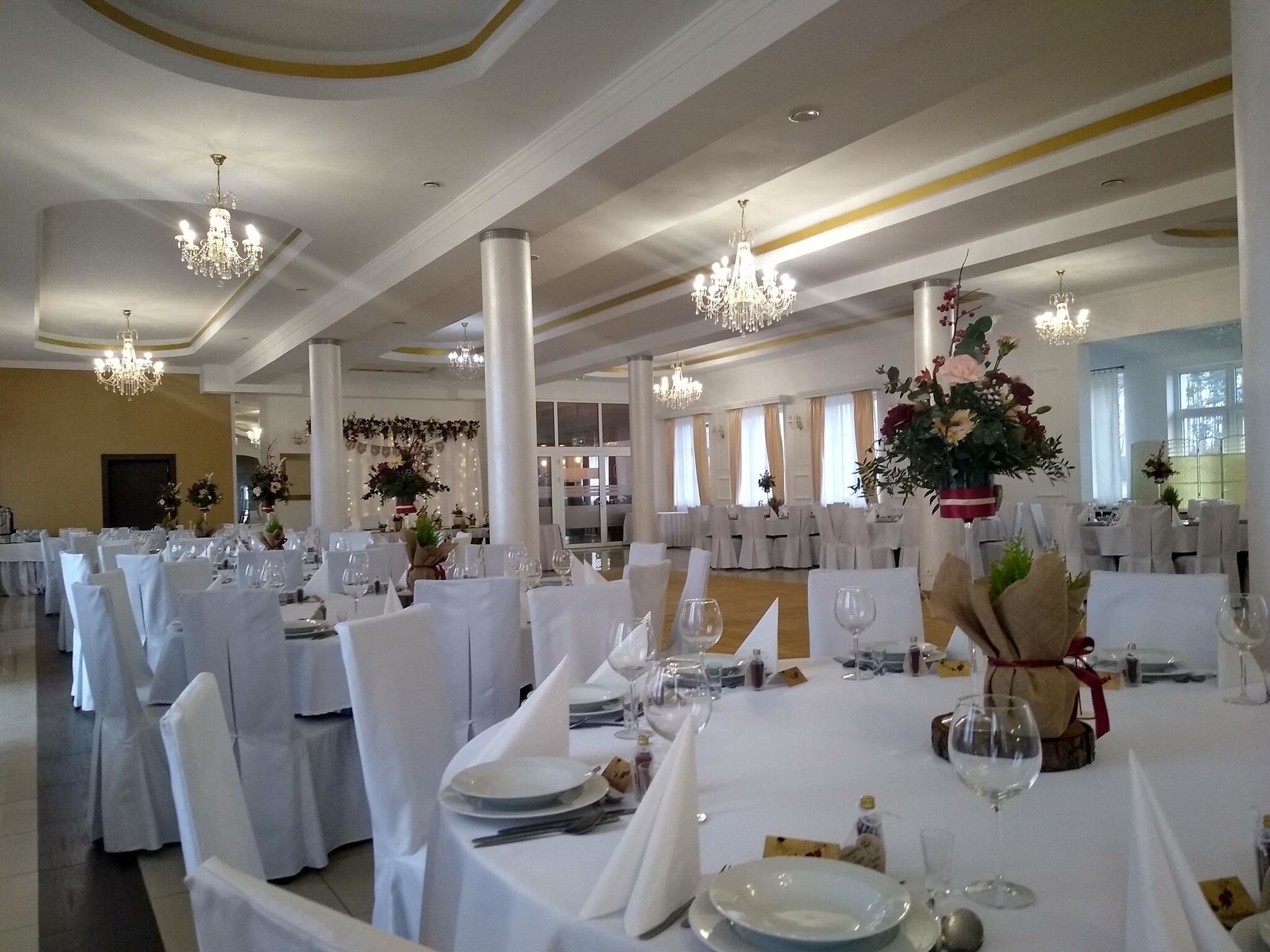 A banquet hall with round tables set for a formal event, featuring white tablecloths, chairs, and centerpieces.