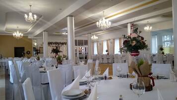 A banquet hall with round tables set for a formal event, featuring white tablecloths, chairs, and centerpieces.