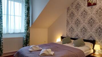 A bedroom with a bed, a nightstand with a lamp, a radiator, and a window with curtains.