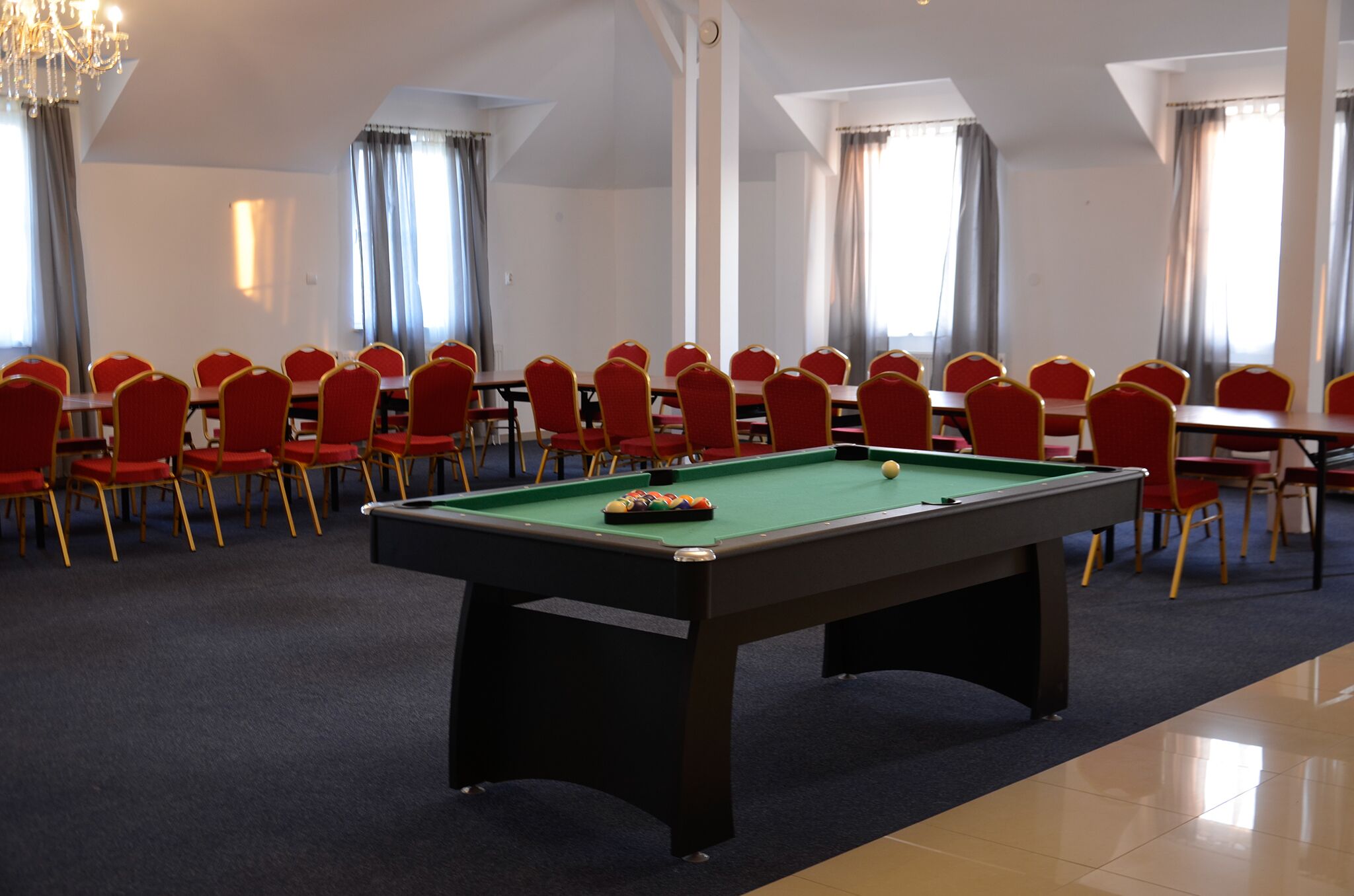 A room with a pool table, red chairs, and a chandelier.
