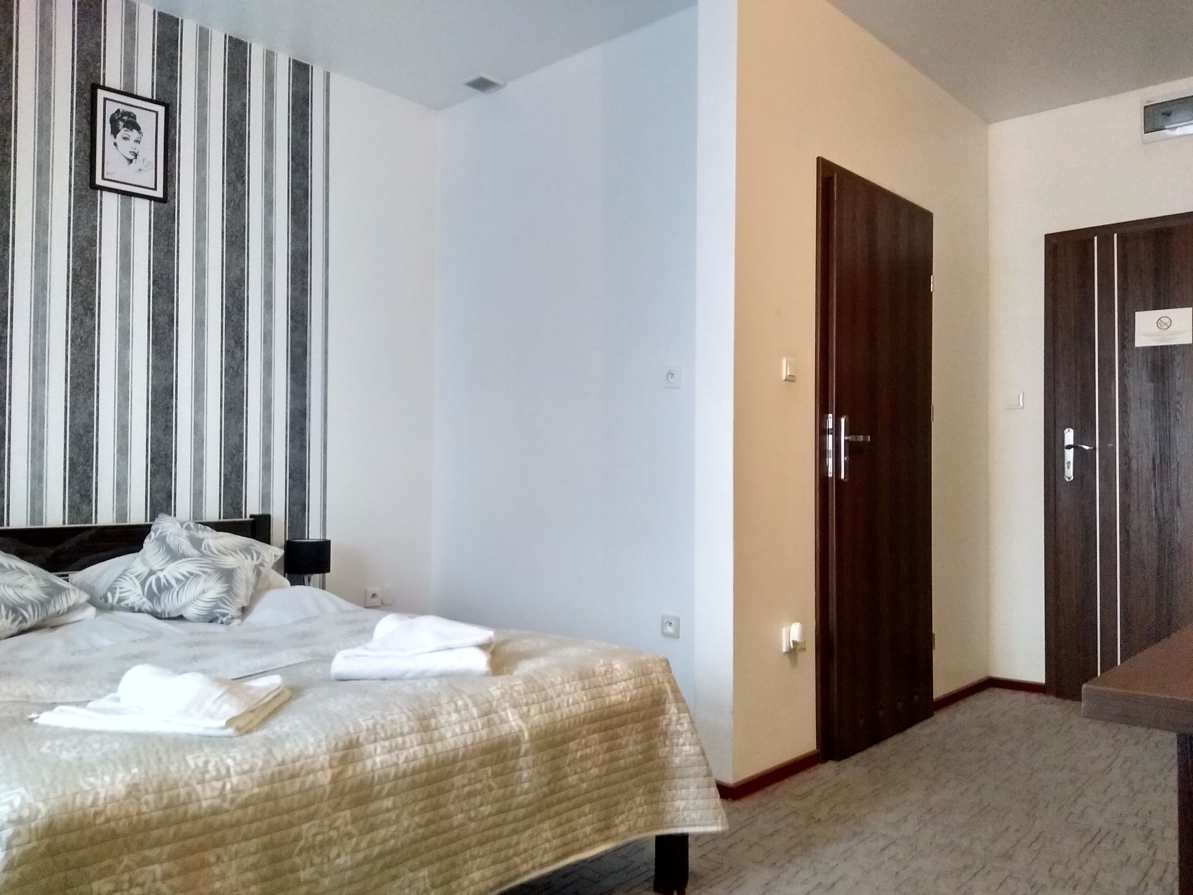 Habitació d'hotel amb un llit, un armari de fusta, una porta i una paret a ratlles.