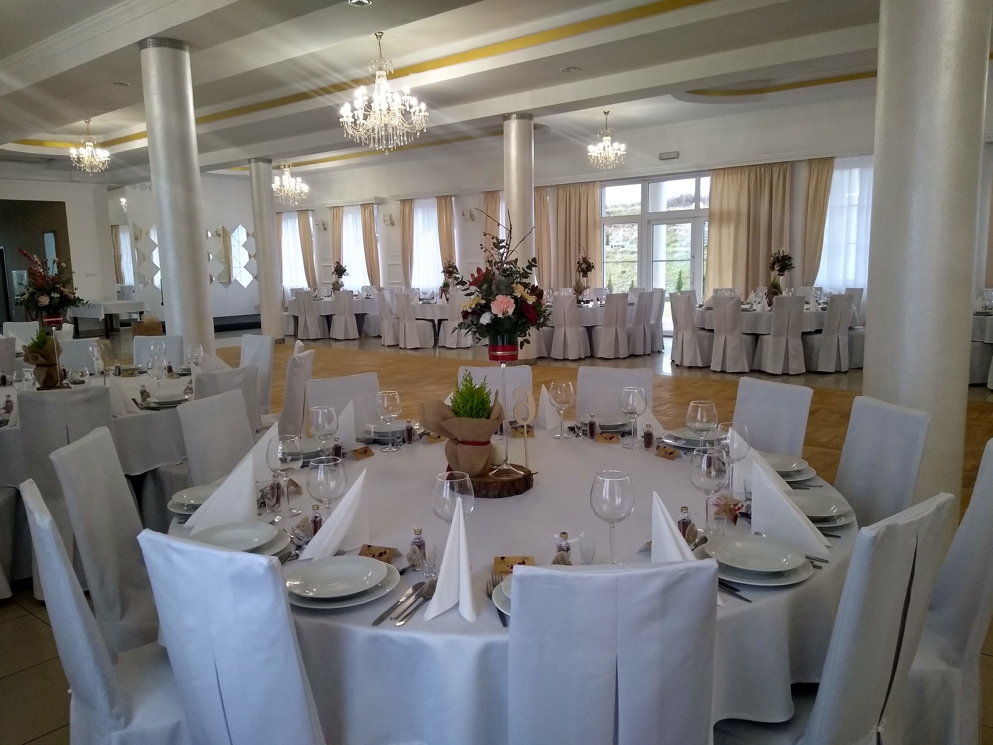 Un salón de banquetes con mesas redondas dispuestas para comer, sillas blancas y candelabros.