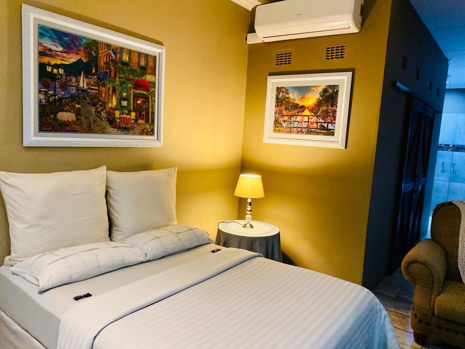 A hotel room with a bed, a nightstand with a lamp, and two framed pictures on the wall.