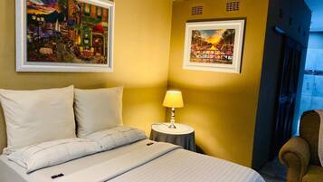A hotel room with a bed, a nightstand with a lamp, and two framed pictures on the wall.
