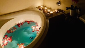 A bathroom with a bathtub filled with water and rose petals, a mirror, and framed floral artwork on the wall. - Rooibos Retreat (Richards Bay)