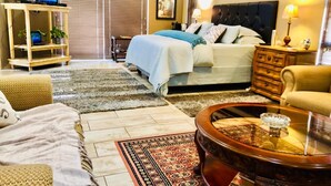 A hotel room with a bed, a TV, a sofa, a coffee table, and a dining table. - Rooibos Retreat (Richards Bay)