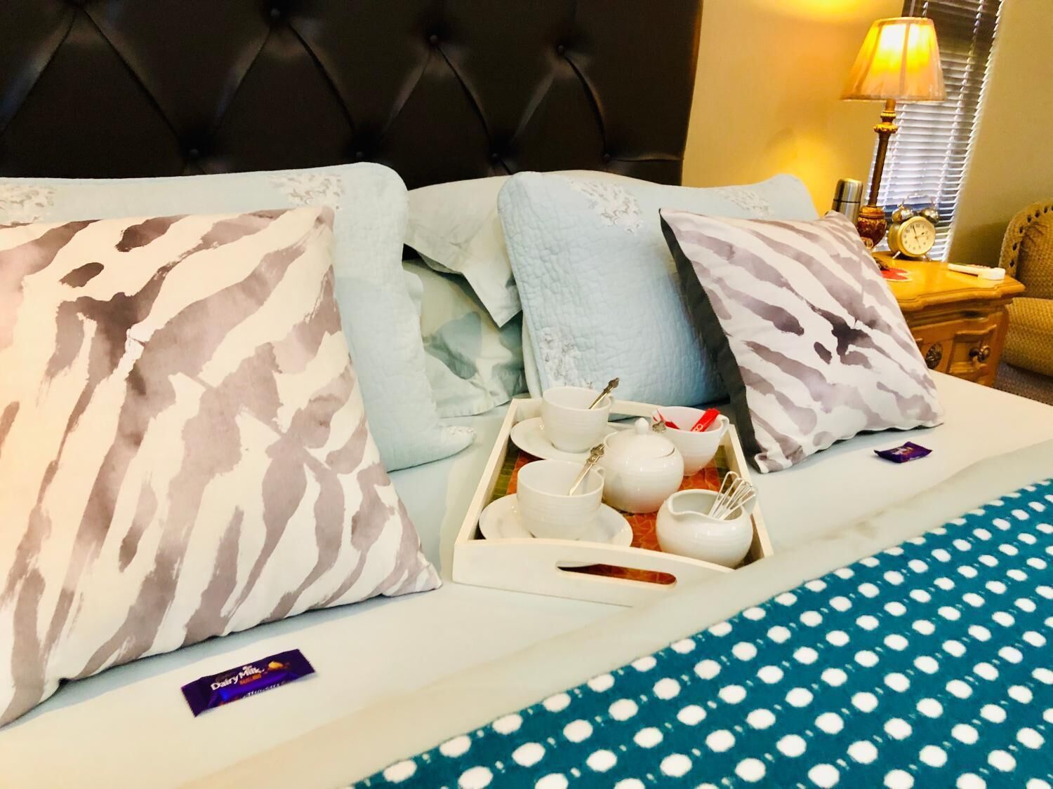 A neatly made bed with patterned pillows, a tray of tea and utensils, and a polka dot bedspread.