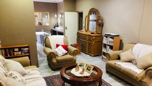 A living room with a sofa, armchair, and a coffee table with a picture frame. There is a dresser and a mirror in the background. - Rooibos Retreat (Richards Bay)