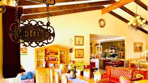 A cozy, well-lit living room with a wooden dining table, chairs, and a red sofa. A 'WELCOME' sign hangs from the ceiling, and there are various framed pictures on the walls. - Rooibos Retreat (Richards Bay)