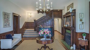 A spacious living room with a grand staircase, a fireplace, and a chandelier. - The West Lane Inn - Queen Room (Ridgefield)