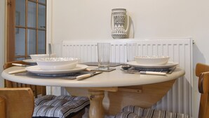 Una mesa de comedor con platos, tazones y cubiertos blancos, frente a una pared blanca con un cuadro enmarcado encima.