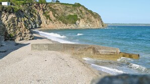 Una costa rocosa con una playa de guijarros y un acantilado con vegetación escasa.