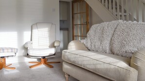 Una sala de estar con un sillón blanco, un sofá color beige y una manta blanca mullida.