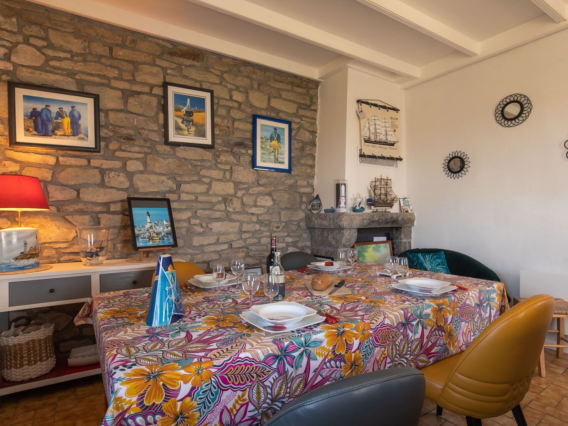 Comedor con pared de piedra, obras de arte enmarcadas, chimenea y mesa lista para dos.